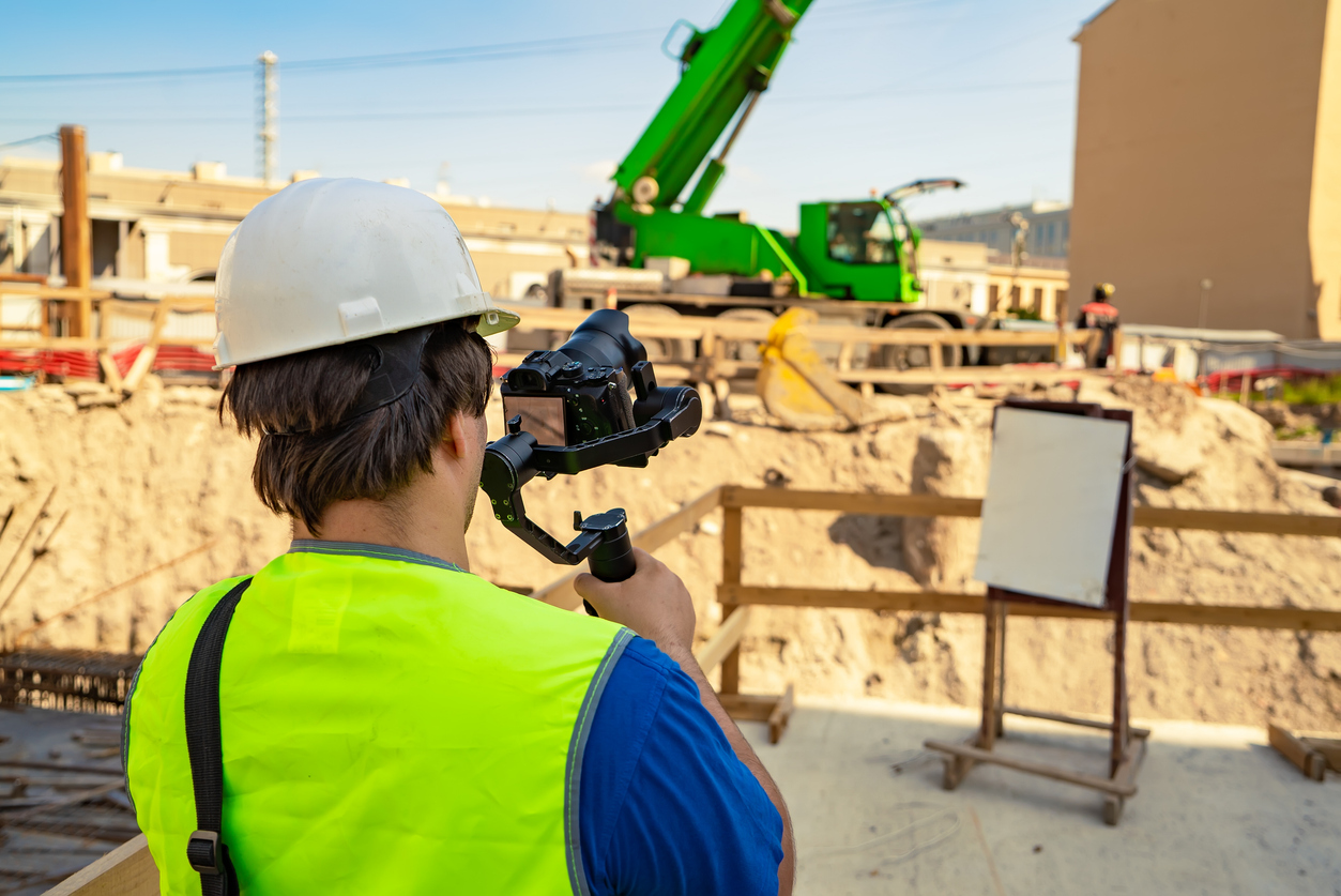 Videographer with a camera and stabilizer in hands filming a working process outdoors. Photographe de chantier
